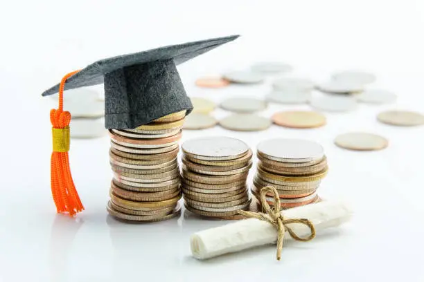 Graduation cap on stacked coins with a tied diploma scroll